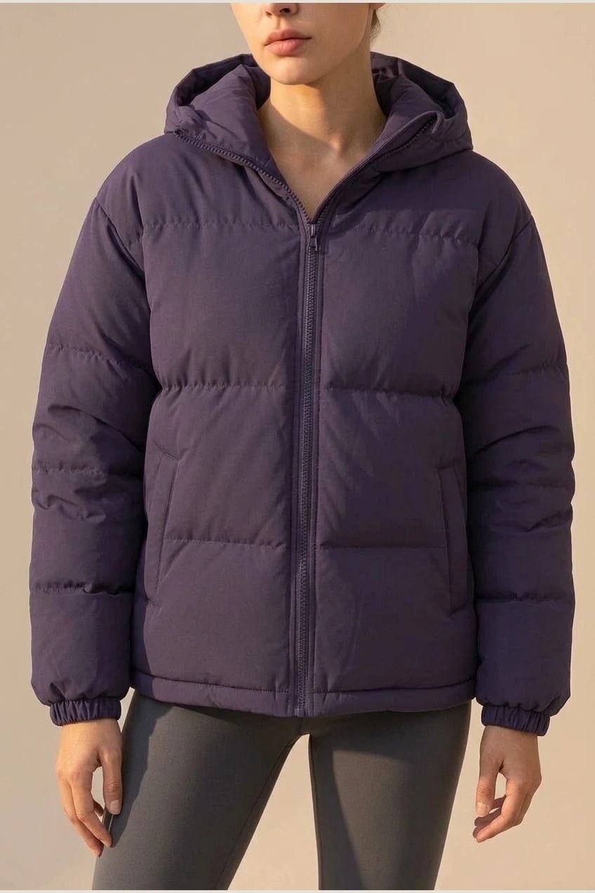 Kvinde i quiltet pufferjakke med hætte, gennemgående lynlås og sidelommer, stylet med smalle bukser og sneakers._2