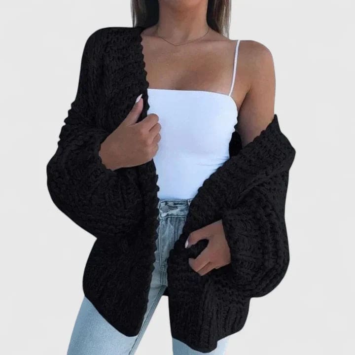 Kvinde iført hvid top, lyse jeans og en sort grovstrikket cardigan med åben front og brede ærmer._0