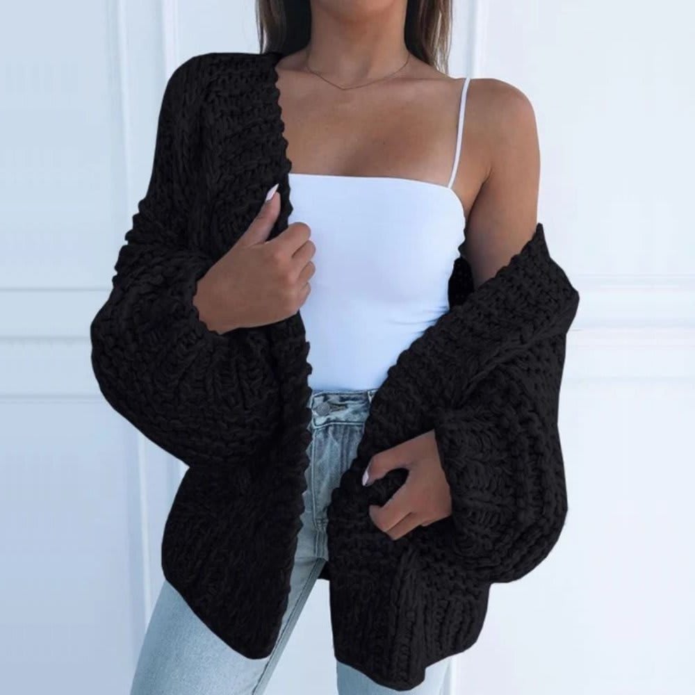 Kvinde iført hvid top, lyse jeans og en sort grovstrikket cardigan med åben front og brede ærmer._4
