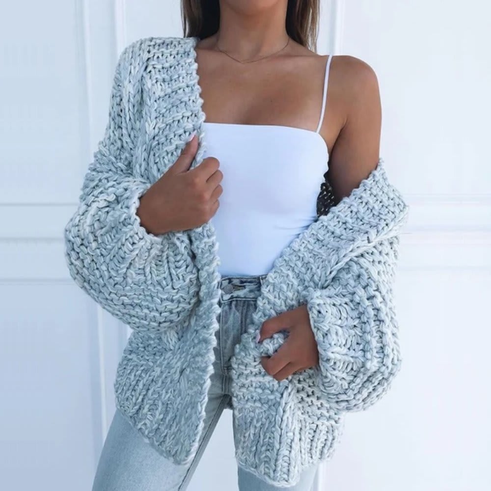 Kvinde iført hvid top, lyse jeans og en sort grovstrikket cardigan med åben front og brede ærmer._7