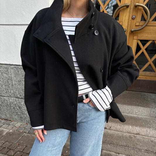 Kvinde iført en sort kort peacoat med høj krave over en stribet top og lyse jeans._0