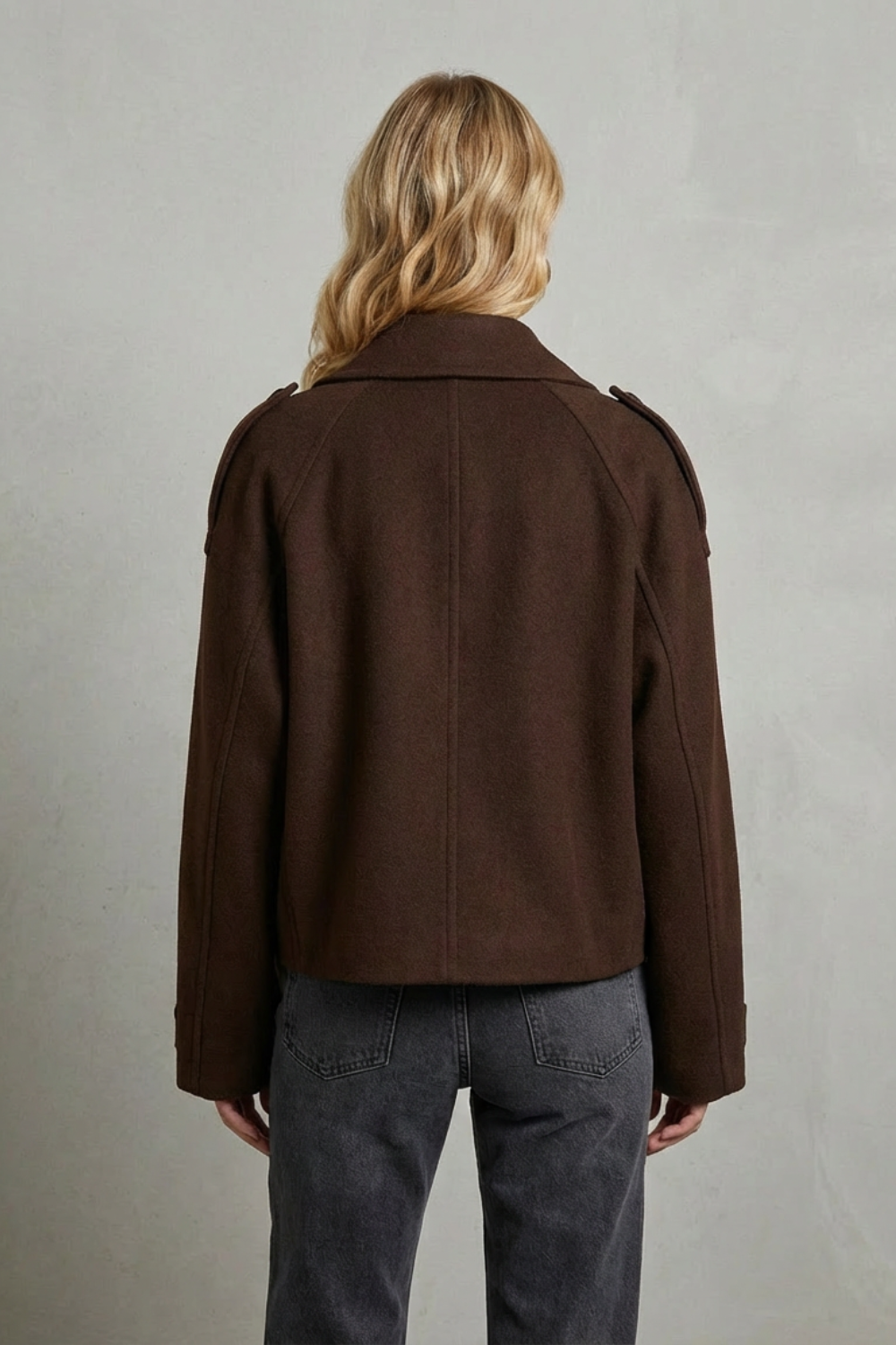Model iført en kortet dobbeltspændt jakke over en beige sweater og mørke jeans, med håndtaske i læder._3