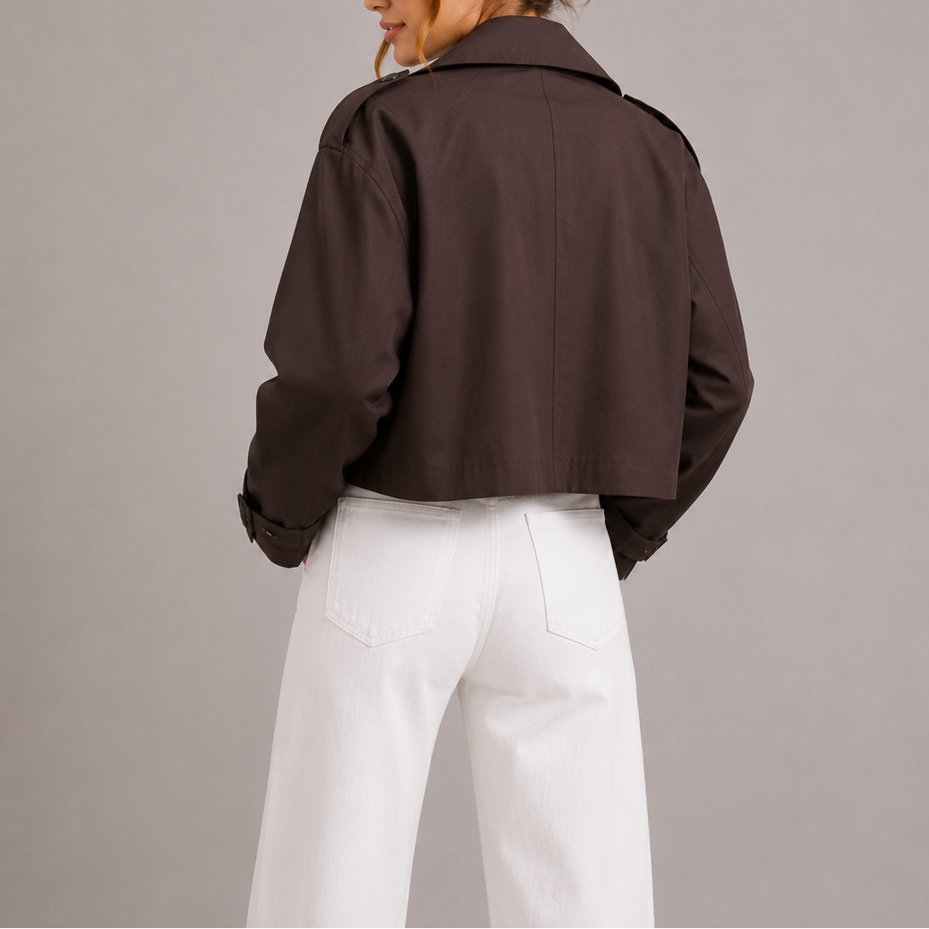 Kvinde iført kortet trenchcoat med oversize revers og dobbeltradede knapper, stylet med hvid top og hvide bukser._1