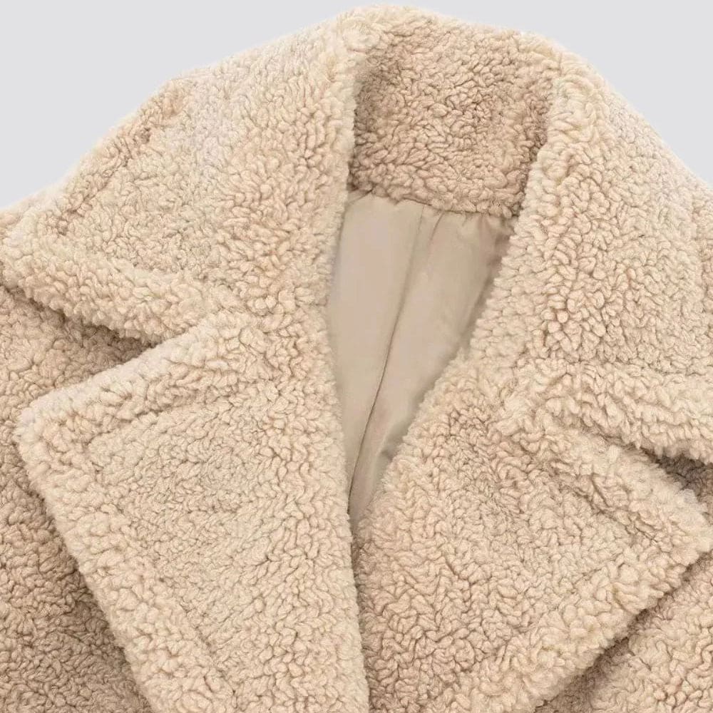 Kvinde iført lang beige teddy-frakke med dobbelt knappelukning og brede revers set forfra_2
