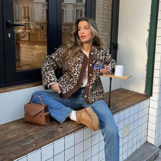 Kvinde iført leopardmønstret cardigan med brunt kontrastpanel og knaplukning over jeans og støvler, siddende på en bænk udenfor en café_0