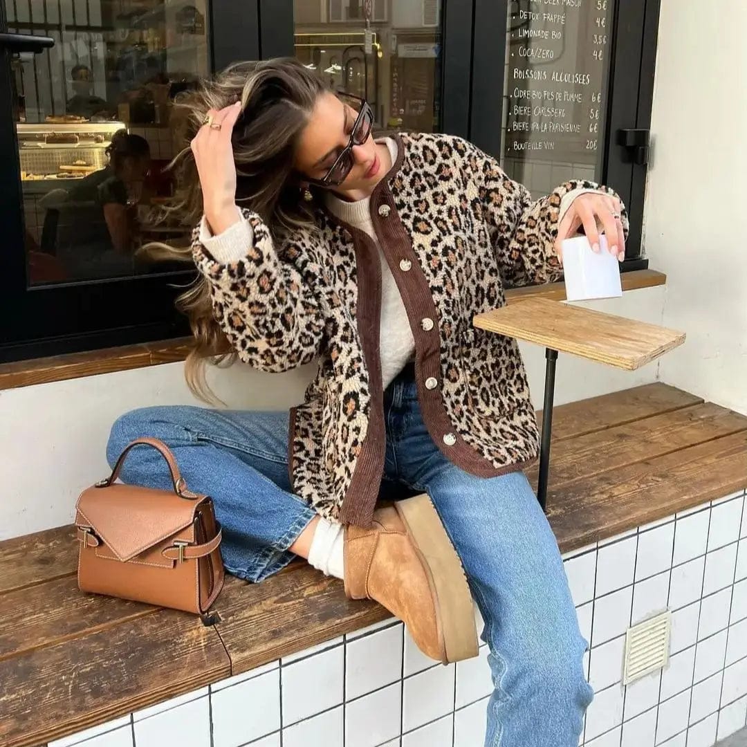 Kvinde iført leopardmønstret cardigan med brunt kontrastpanel og knaplukning over jeans og støvler, siddende på en bænk udenfor en café_1