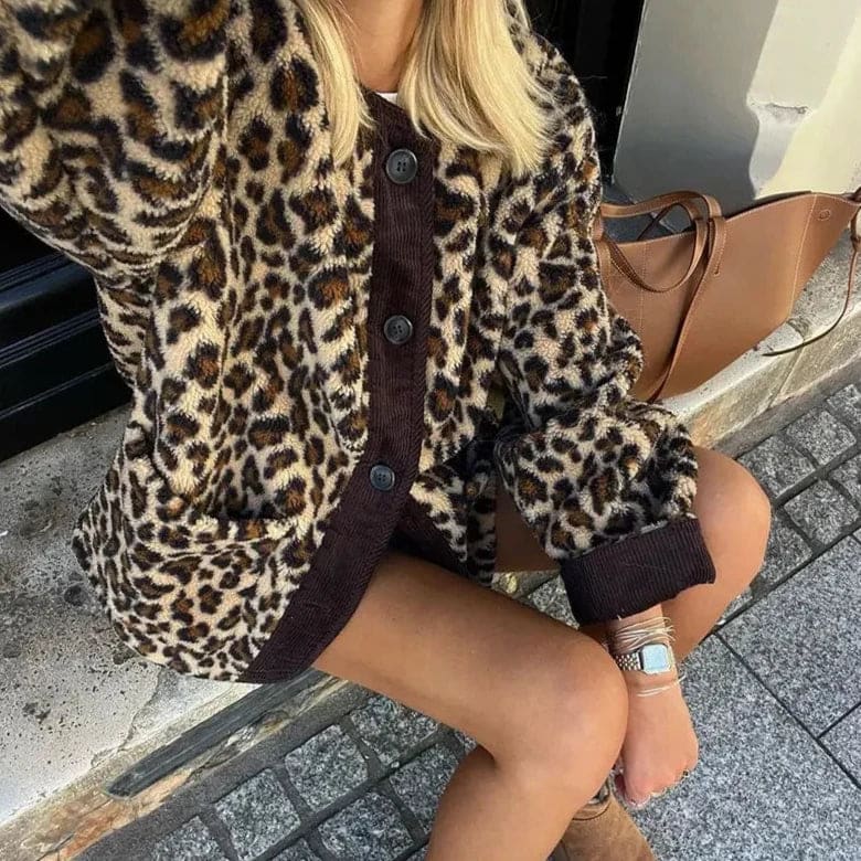 Kvinde iført leopardmønstret cardigan med brunt kontrastpanel og knaplukning over jeans og støvler, siddende på en bænk udenfor en café_4