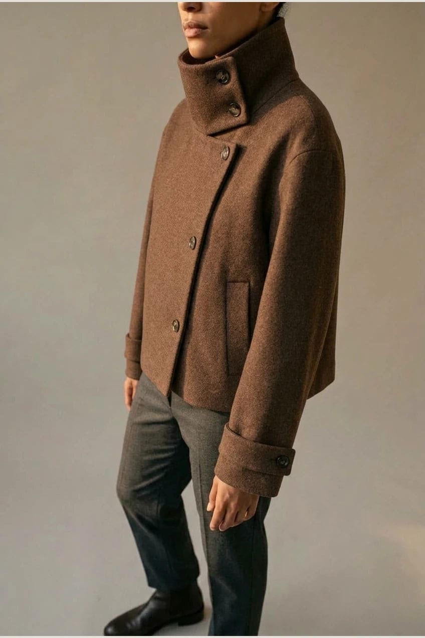 Kort jakke med høj krave, spændelukning foroven, knapper foran og manchetter med rem, båret over striktrøje og lige bukser._22
