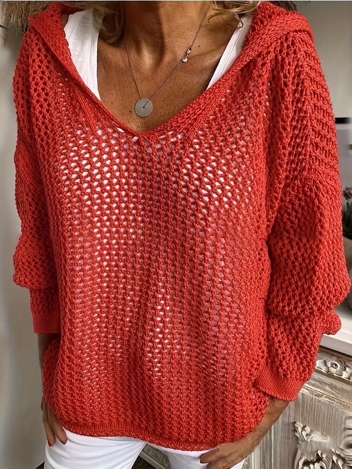 Kvinde iført en løst strikket sweater med åben struktur og hætte, stylet over en hvid bluse_0
