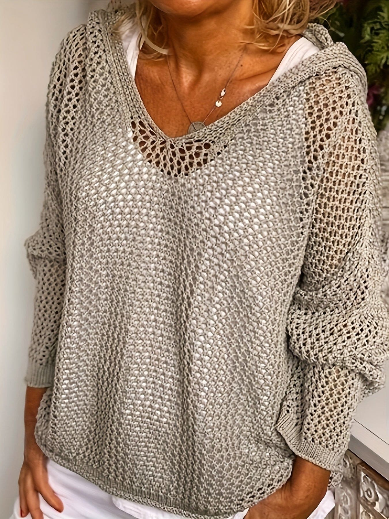 Kvinde iført en løst strikket sweater med åben struktur og hætte, stylet over en hvid bluse_2