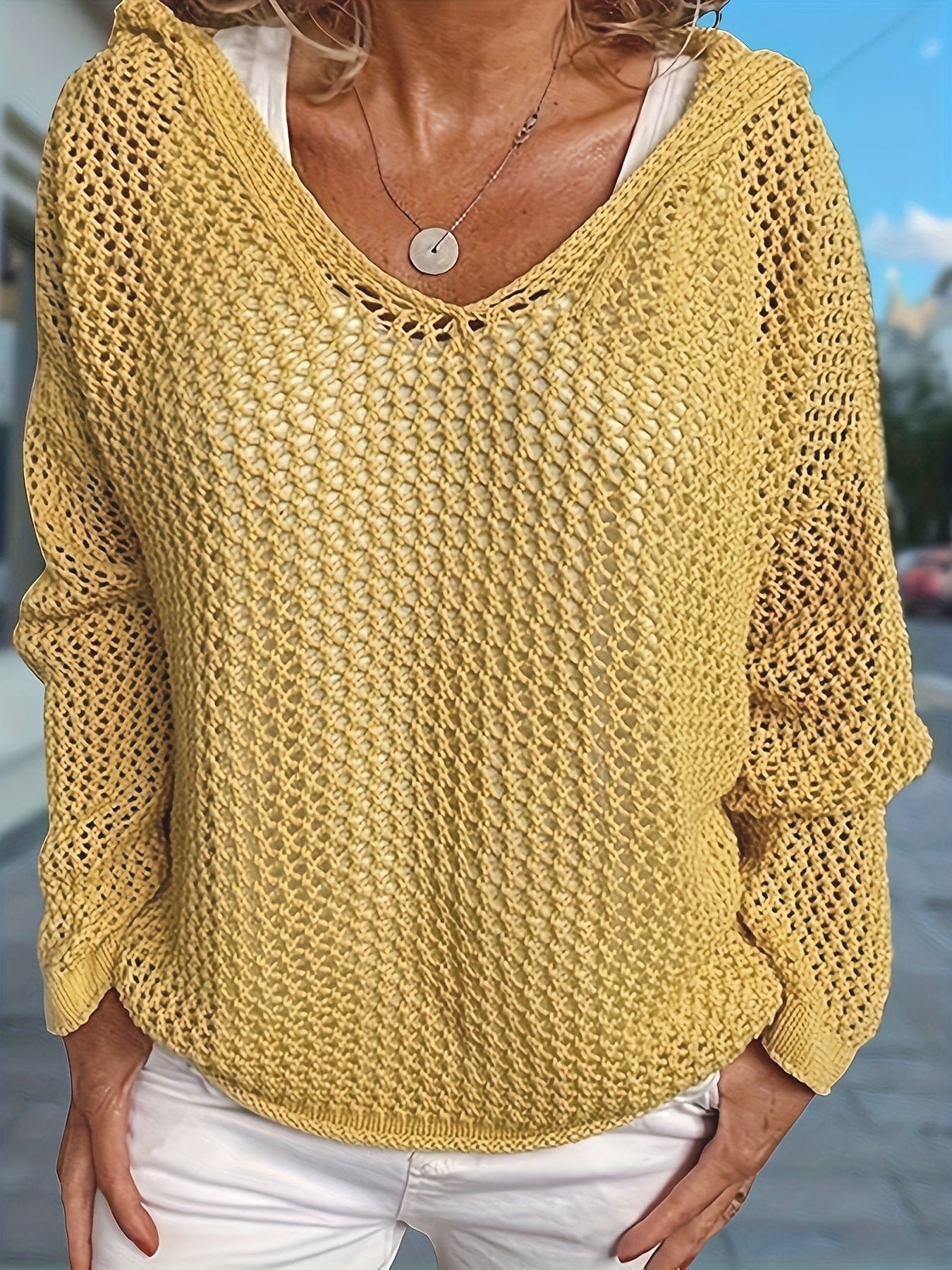 Kvinde iført en løst strikket sweater med åben struktur og hætte, stylet over en hvid bluse_3