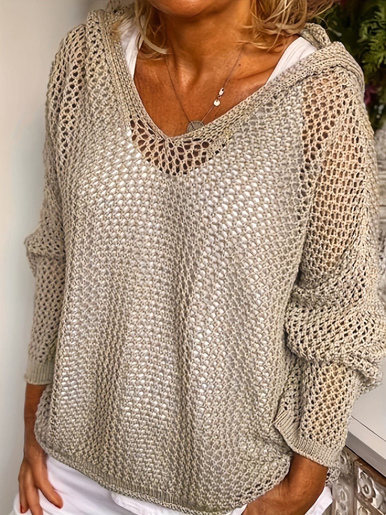 Kvinde iført en løst strikket sweater med åben struktur og hætte, stylet over en hvid bluse_4