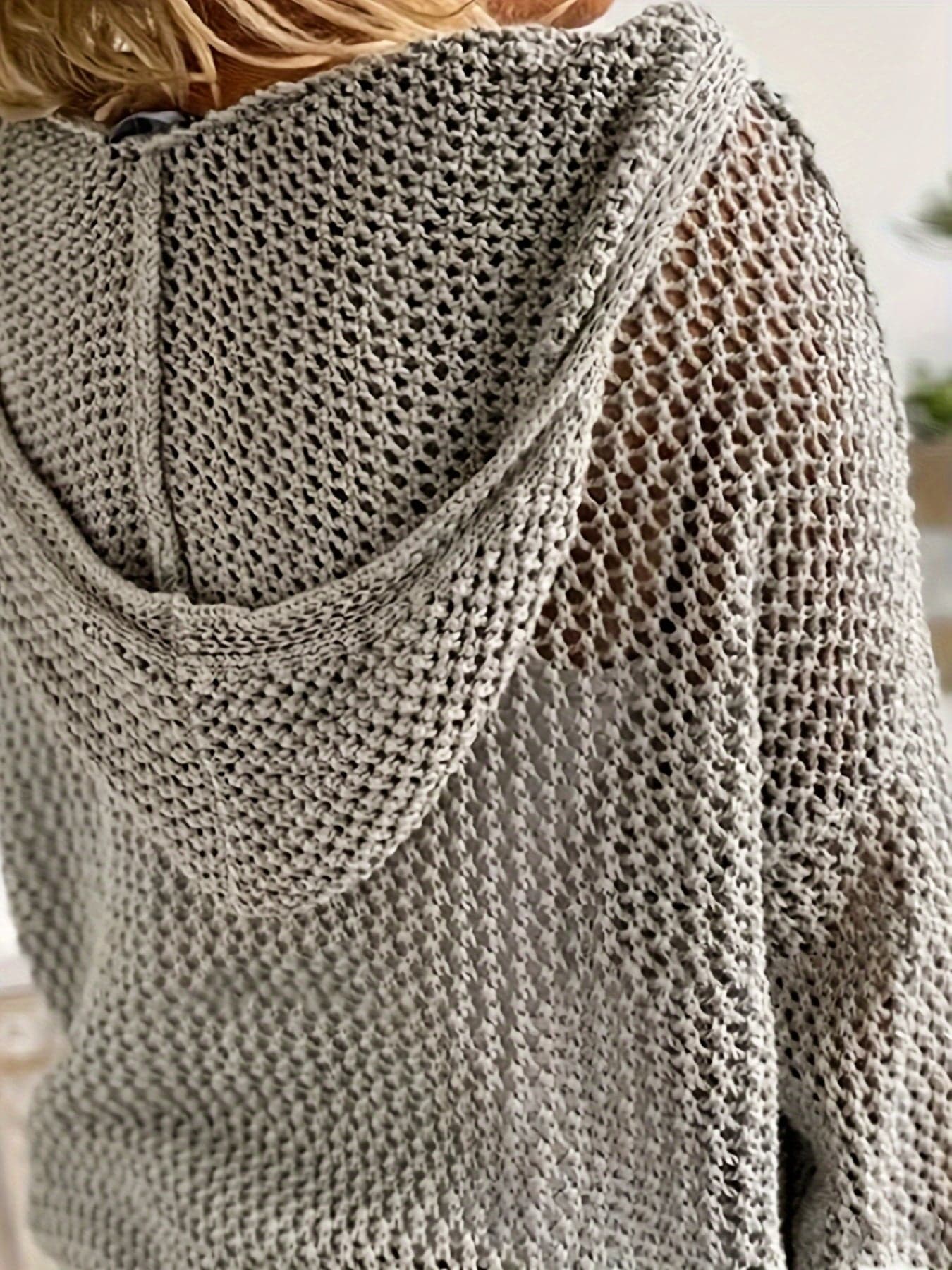 Kvinde iført en løst strikket sweater med åben struktur og hætte, stylet over en hvid bluse_7