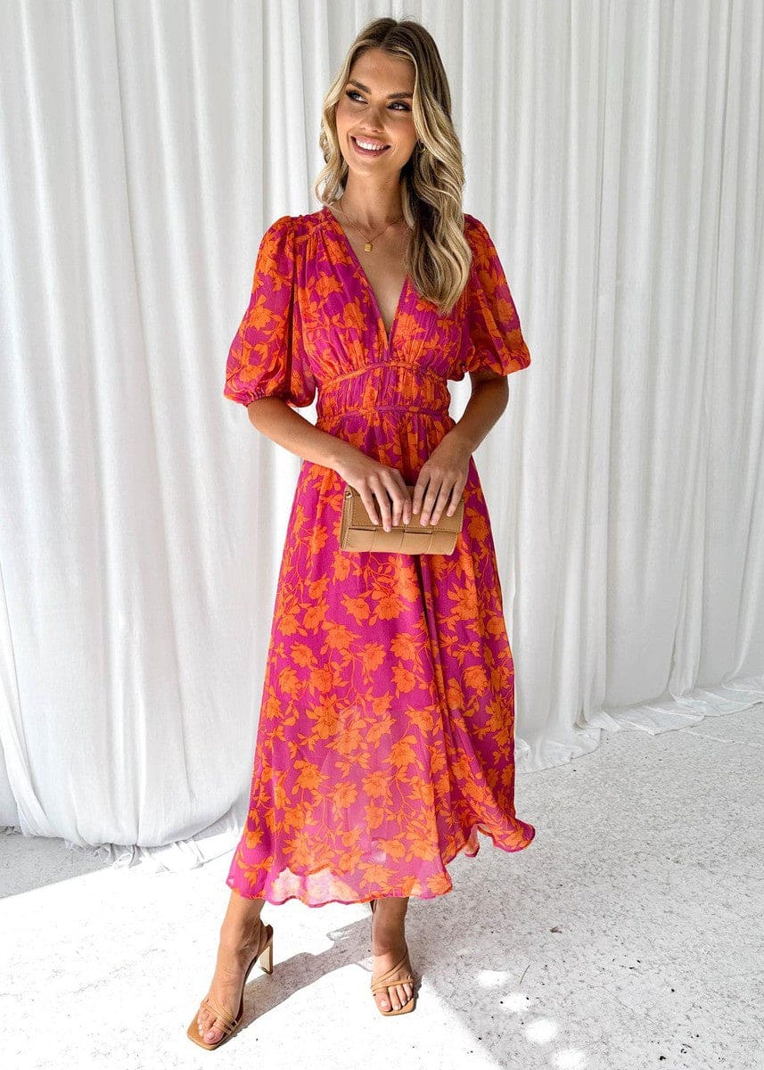 Kvinde iført en maxi kjole med orange og pink blomsterprint, v-udskæring og ballon-ærmer, perfekt til bryllup og festlige begivenheder._1