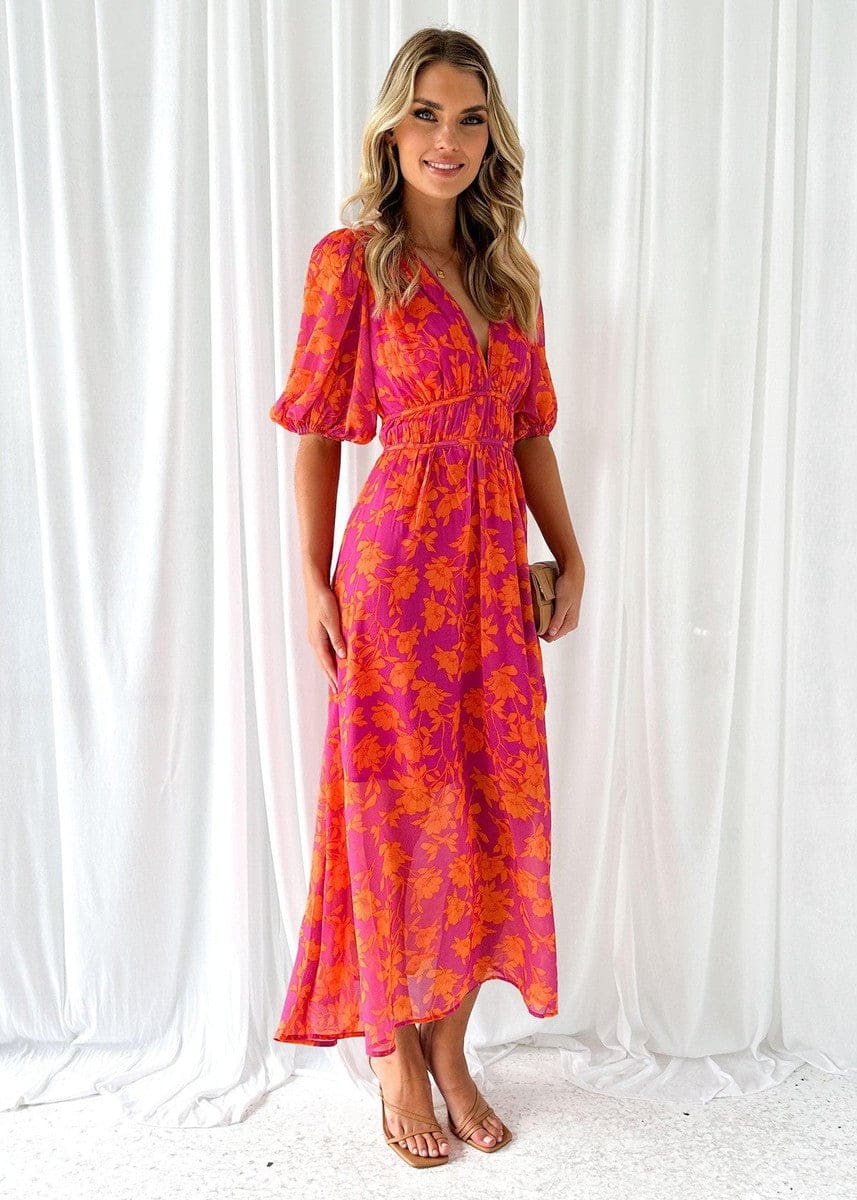 Kvinde iført en maxi kjole med orange og pink blomsterprint, v-udskæring og ballon-ærmer, perfekt til bryllup og festlige begivenheder._2