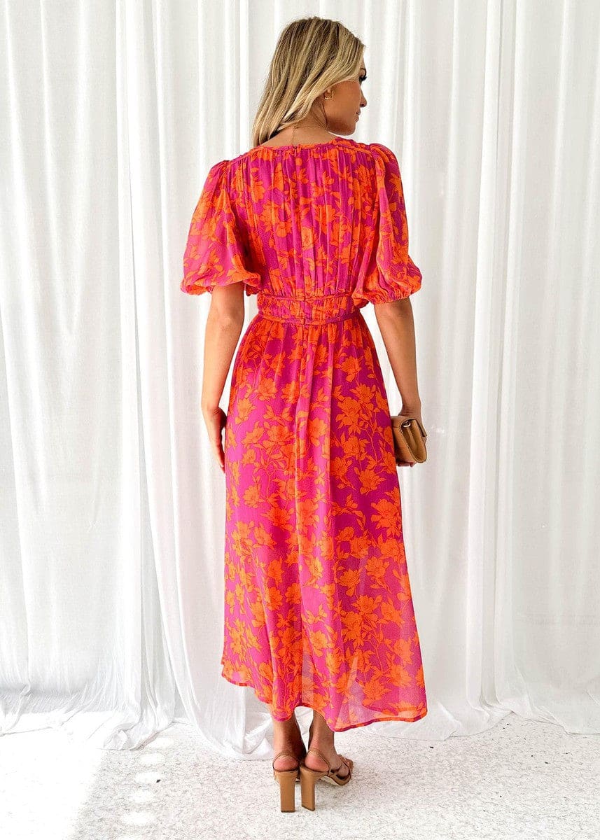 Kvinde iført en maxi kjole med orange og pink blomsterprint, v-udskæring og ballon-ærmer, perfekt til bryllup og festlige begivenheder._3