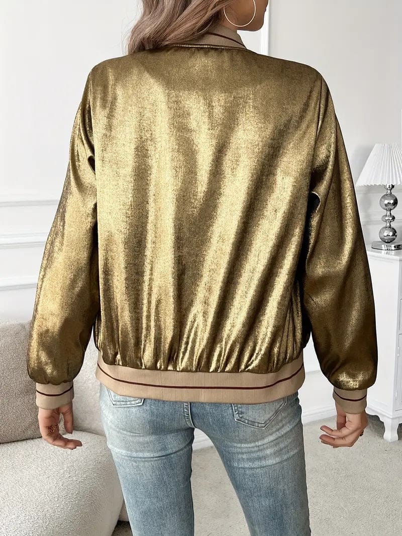 Kvinde iført en guldfarvet metallic bomberjakke med lynlås og ribkant, kombineret med hvid top og jeans._1