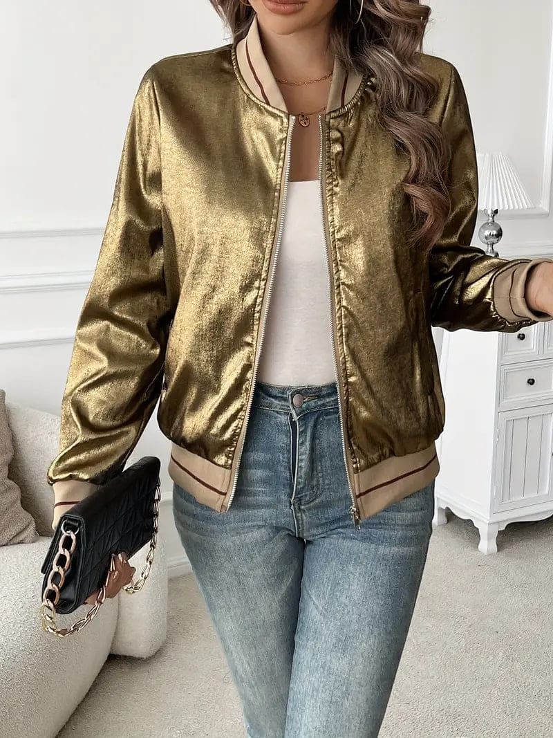 Kvinde iført en guldfarvet metallic bomberjakke med lynlås og ribkant, kombineret med hvid top og jeans._2