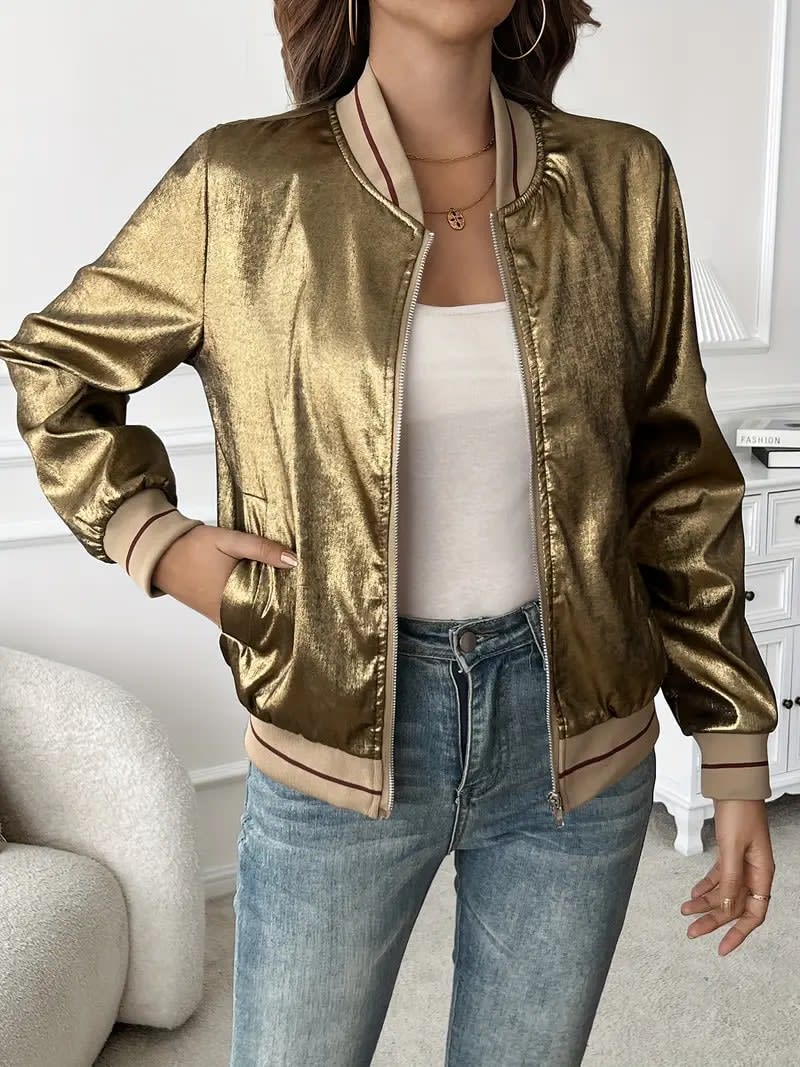 Kvinde iført en guldfarvet metallic bomberjakke med lynlås og ribkant, kombineret med hvid top og jeans._3