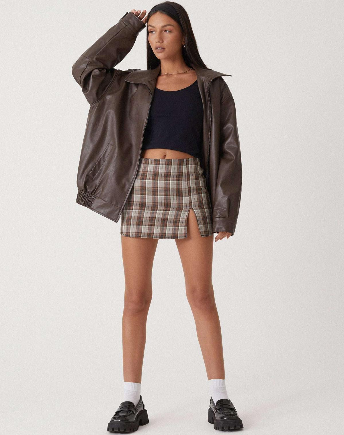 Model iført en oversize jakke med krave, lynlås og drop-skuldre, styling med sort top og ternet nederdel._1