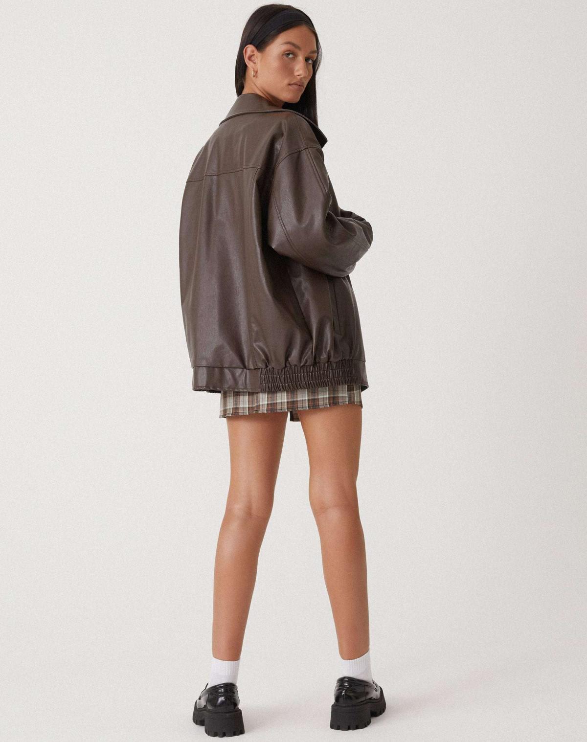 Model iført en oversize jakke med krave, lynlås og drop-skuldre, styling med sort top og ternet nederdel._3