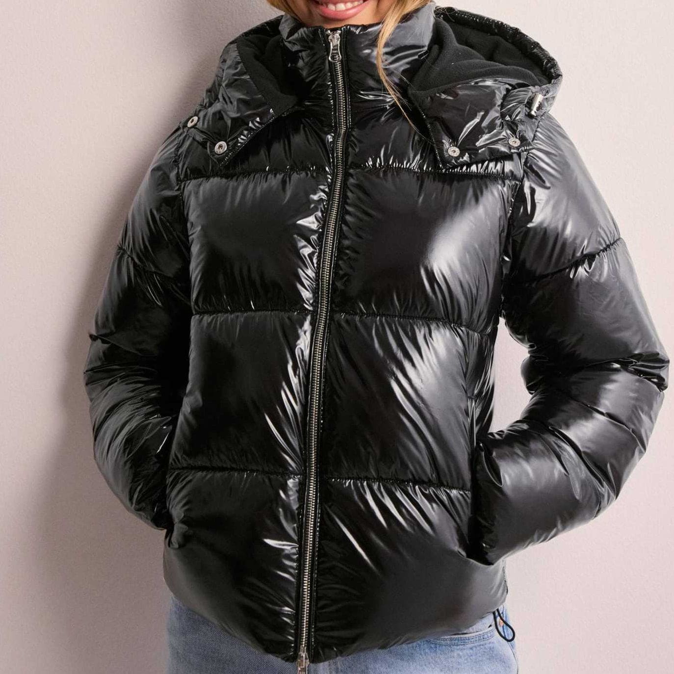 Kvinde iført sort quiltet pufferjakke med hætte og lynlås foran, stylet med hvid top og lyse jeans_1