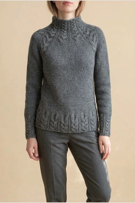 Kvinde i strikket sweater med høj hals, raglanærmer og snoningsmønster ved skuldre og nederste kant._0