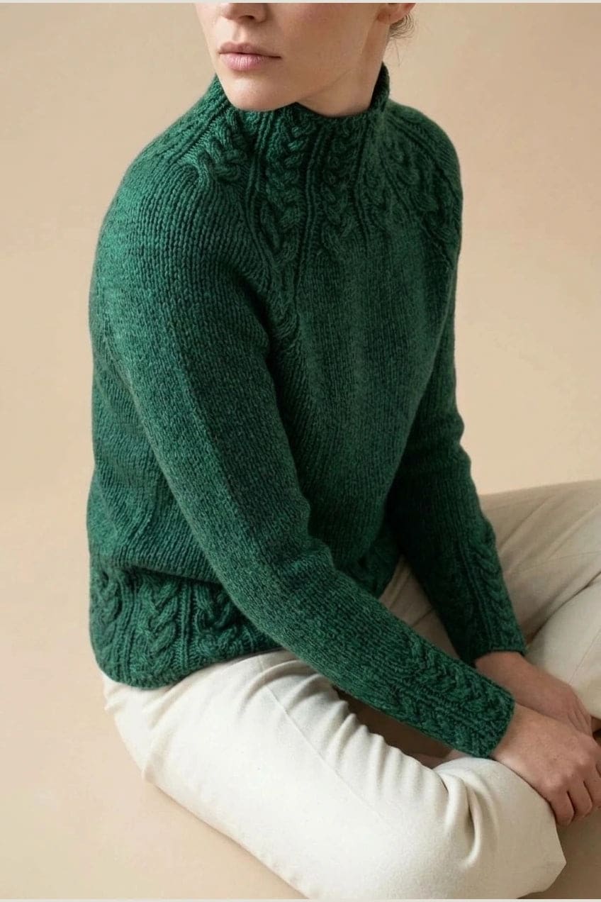 Kvinde i strikket sweater med høj hals, raglanærmer og snoningsmønster ved skuldre og nederste kant._10