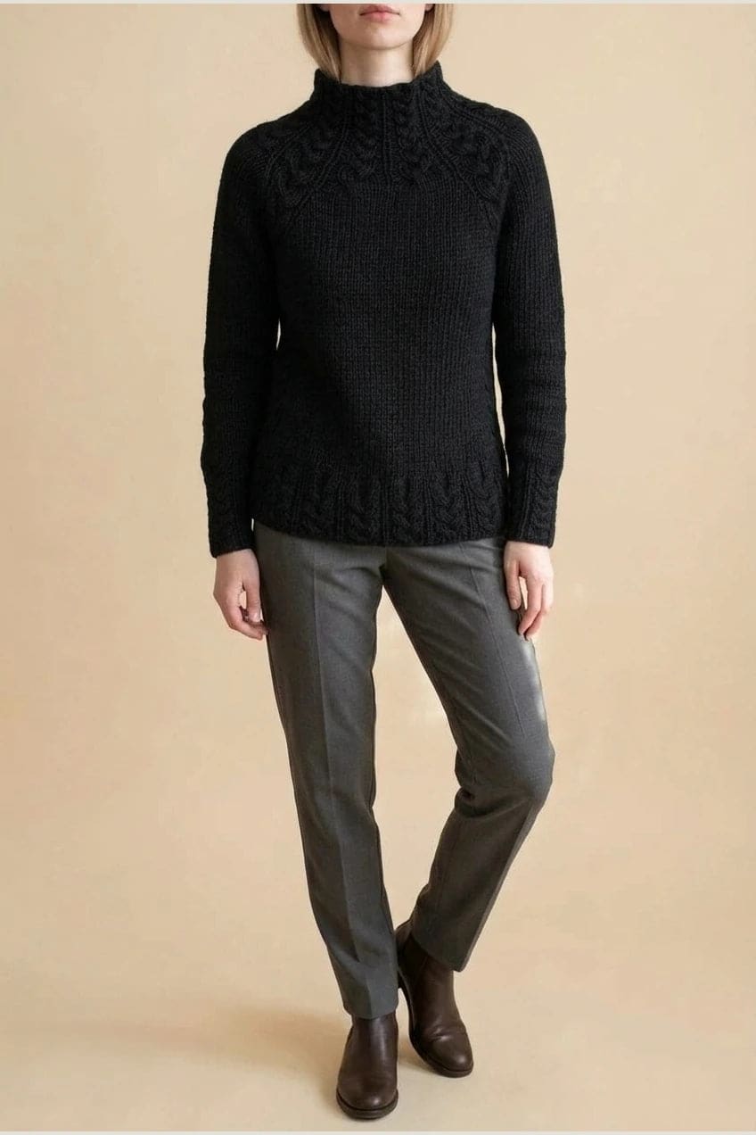 Kvinde i strikket sweater med høj hals, raglanærmer og snoningsmønster ved skuldre og nederste kant._13