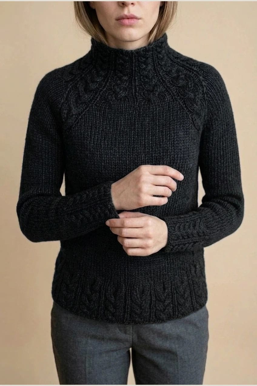 Kvinde i strikket sweater med høj hals, raglanærmer og snoningsmønster ved skuldre og nederste kant._14
