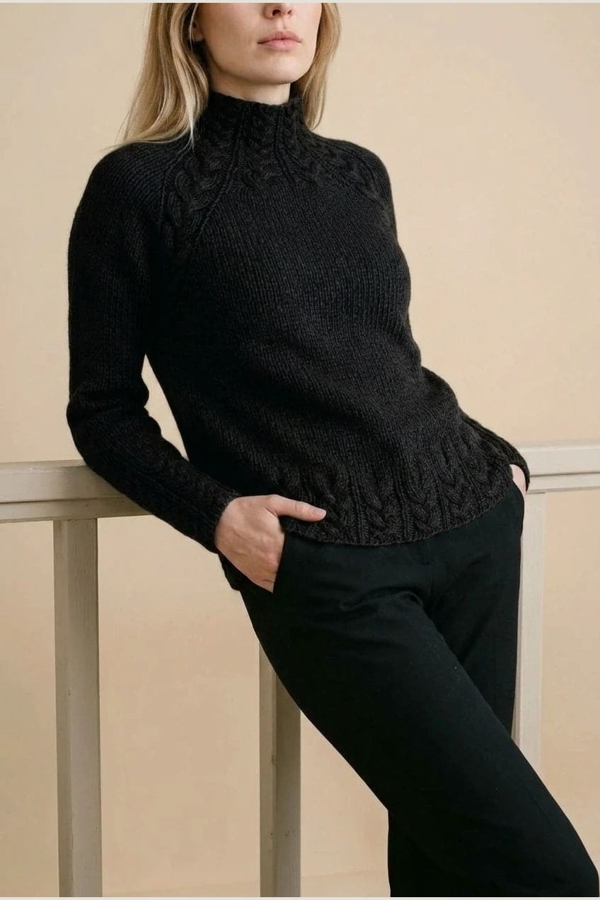Kvinde i strikket sweater med høj hals, raglanærmer og snoningsmønster ved skuldre og nederste kant._15
