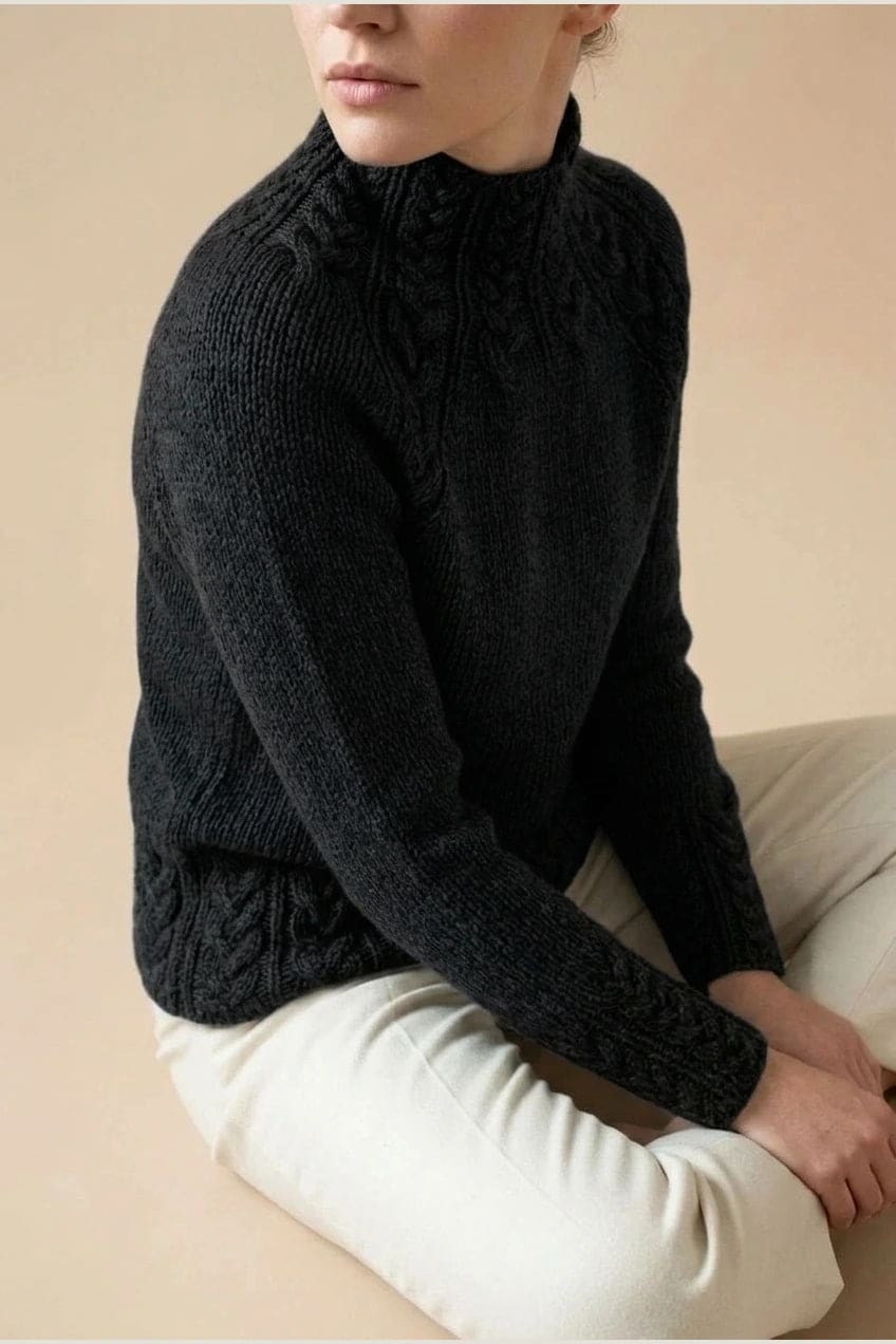 Kvinde i strikket sweater med høj hals, raglanærmer og snoningsmønster ved skuldre og nederste kant._16