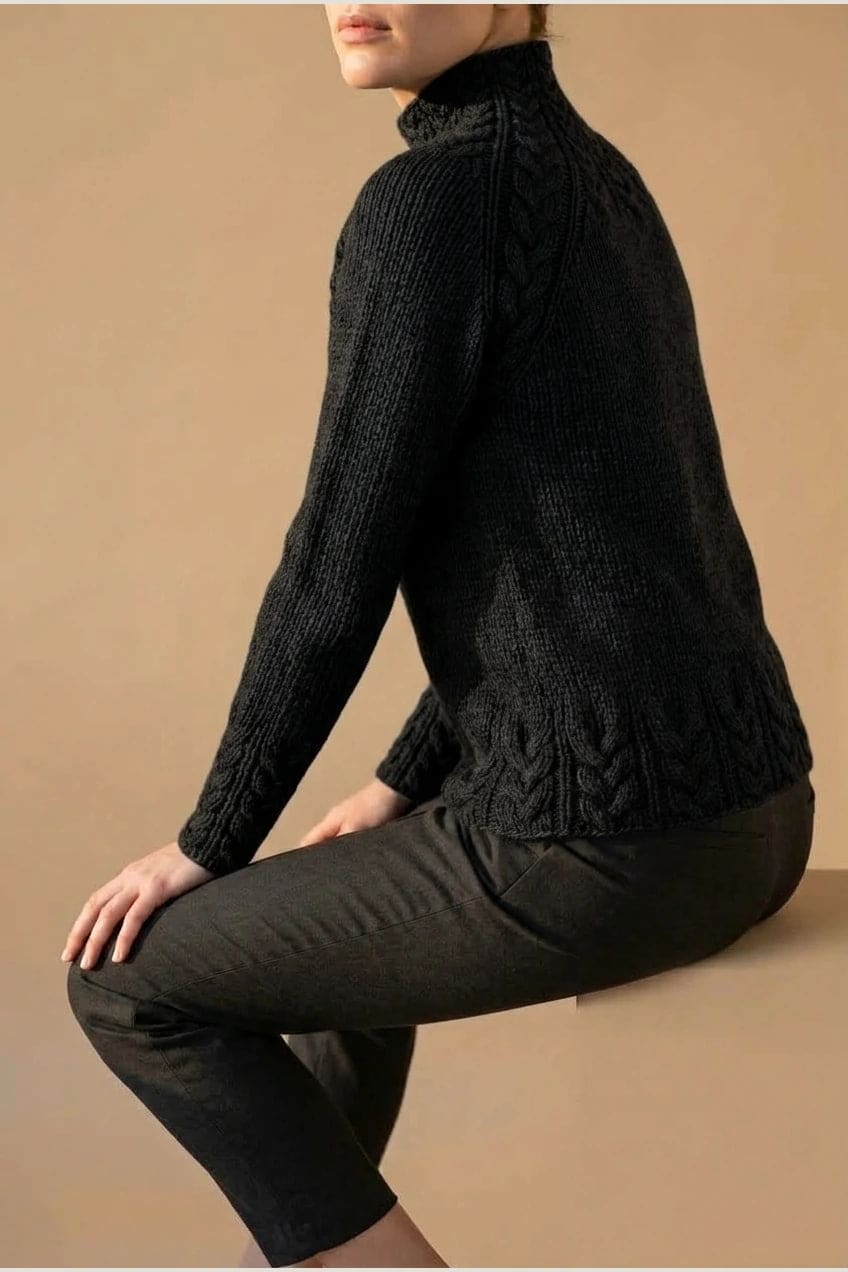 Kvinde i strikket sweater med høj hals, raglanærmer og snoningsmønster ved skuldre og nederste kant._17