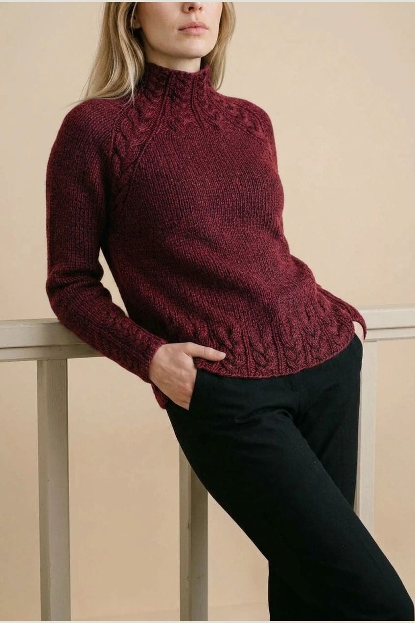 Kvinde i strikket sweater med høj hals, raglanærmer og snoningsmønster ved skuldre og nederste kant._21