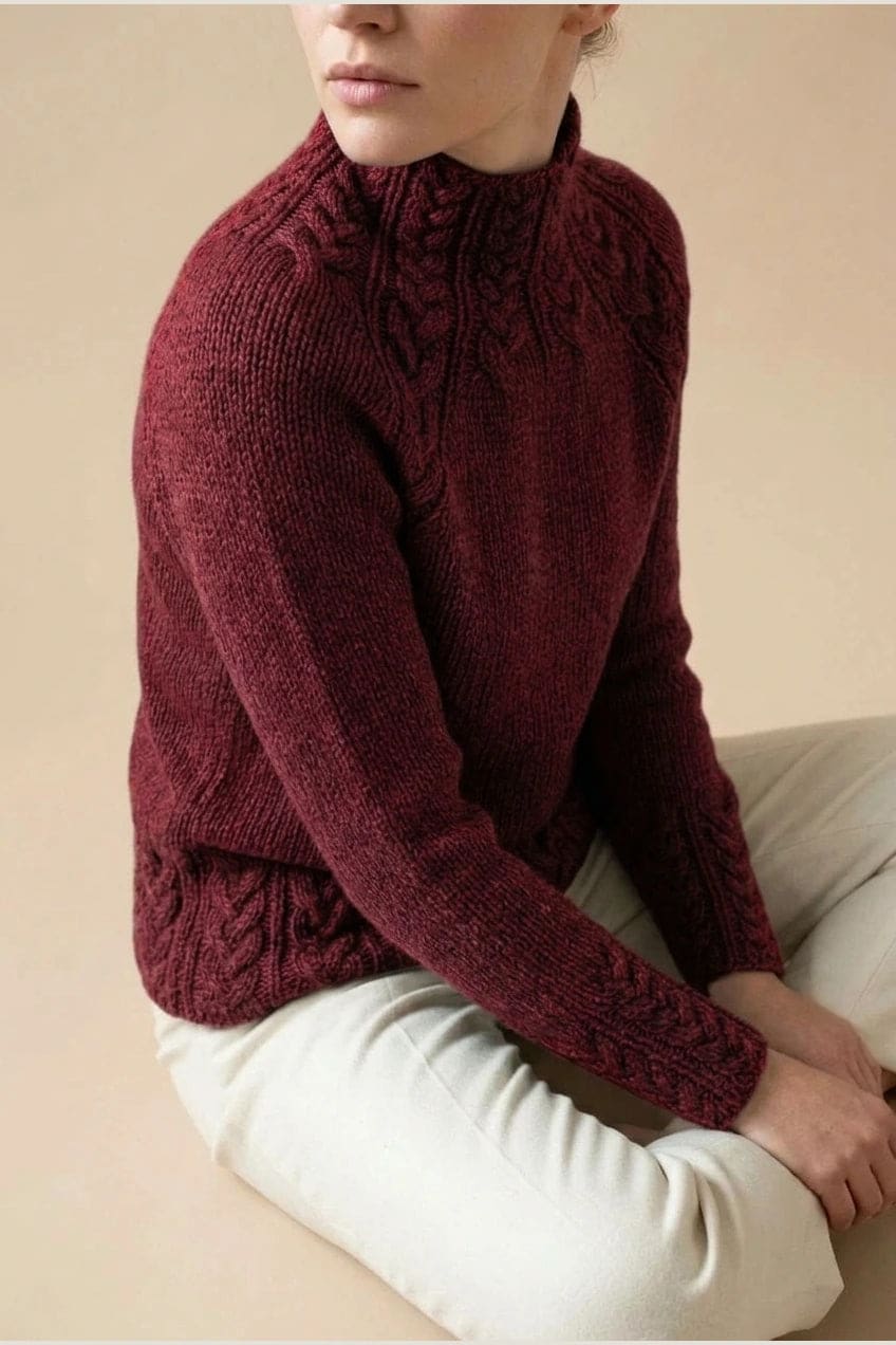Kvinde i strikket sweater med høj hals, raglanærmer og snoningsmønster ved skuldre og nederste kant._22