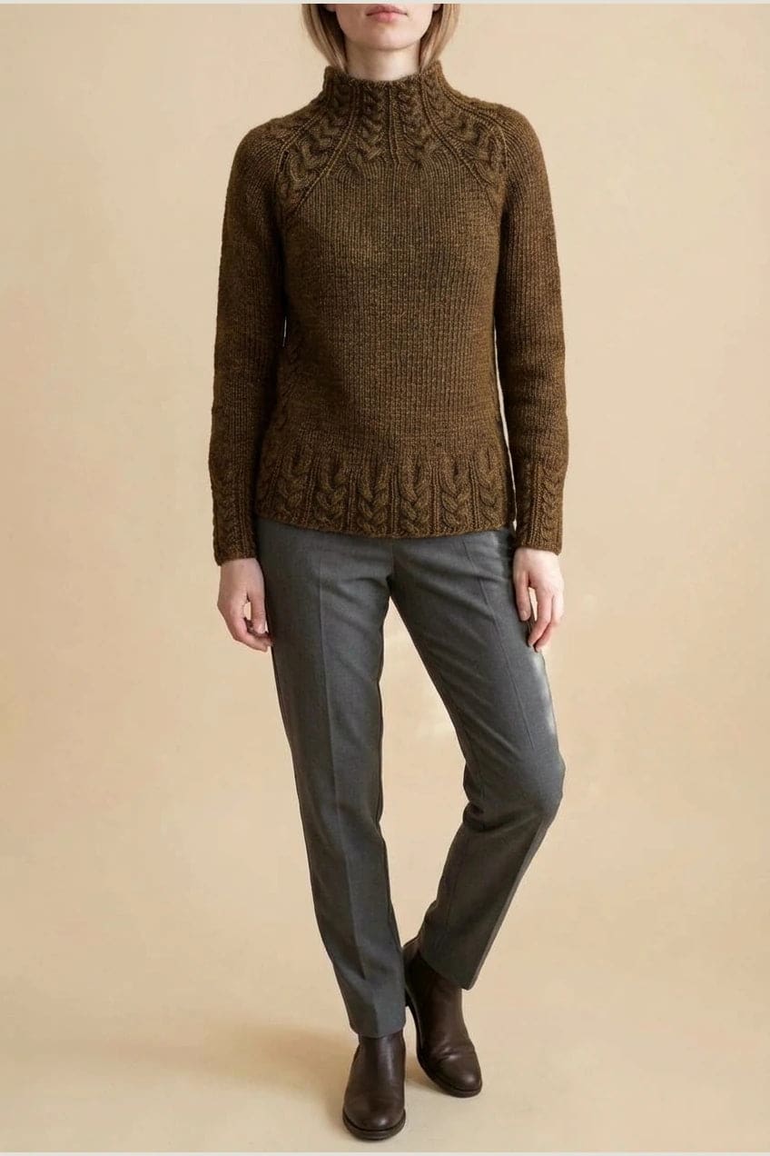 Kvinde i strikket sweater med høj hals, raglanærmer og snoningsmønster ved skuldre og nederste kant._25