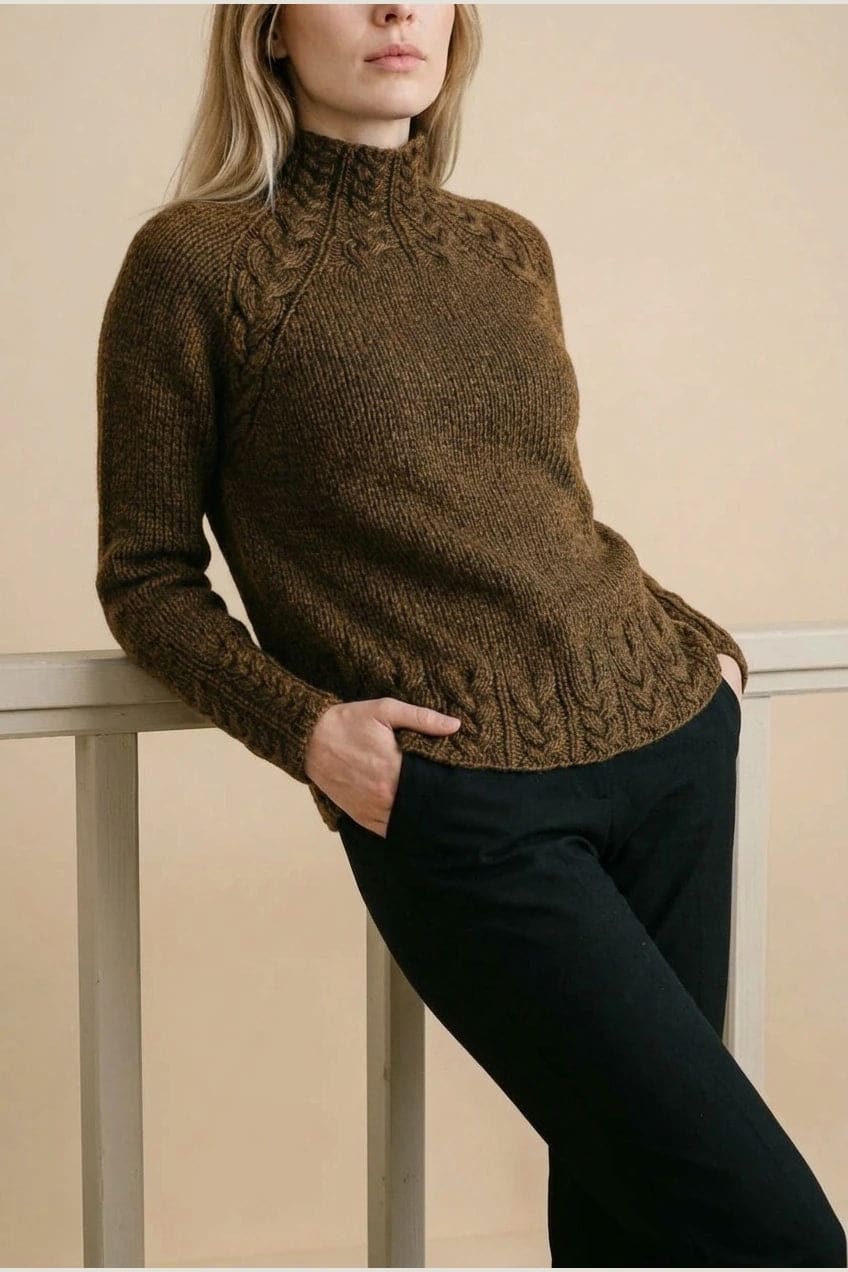 Kvinde i strikket sweater med høj hals, raglanærmer og snoningsmønster ved skuldre og nederste kant._27