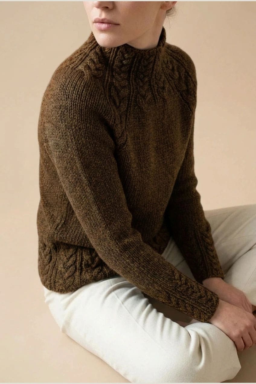 Kvinde i strikket sweater med høj hals, raglanærmer og snoningsmønster ved skuldre og nederste kant._28