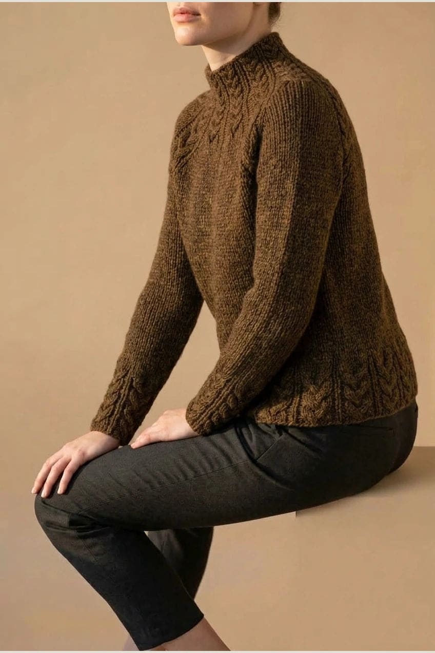 Kvinde i strikket sweater med høj hals, raglanærmer og snoningsmønster ved skuldre og nederste kant._29