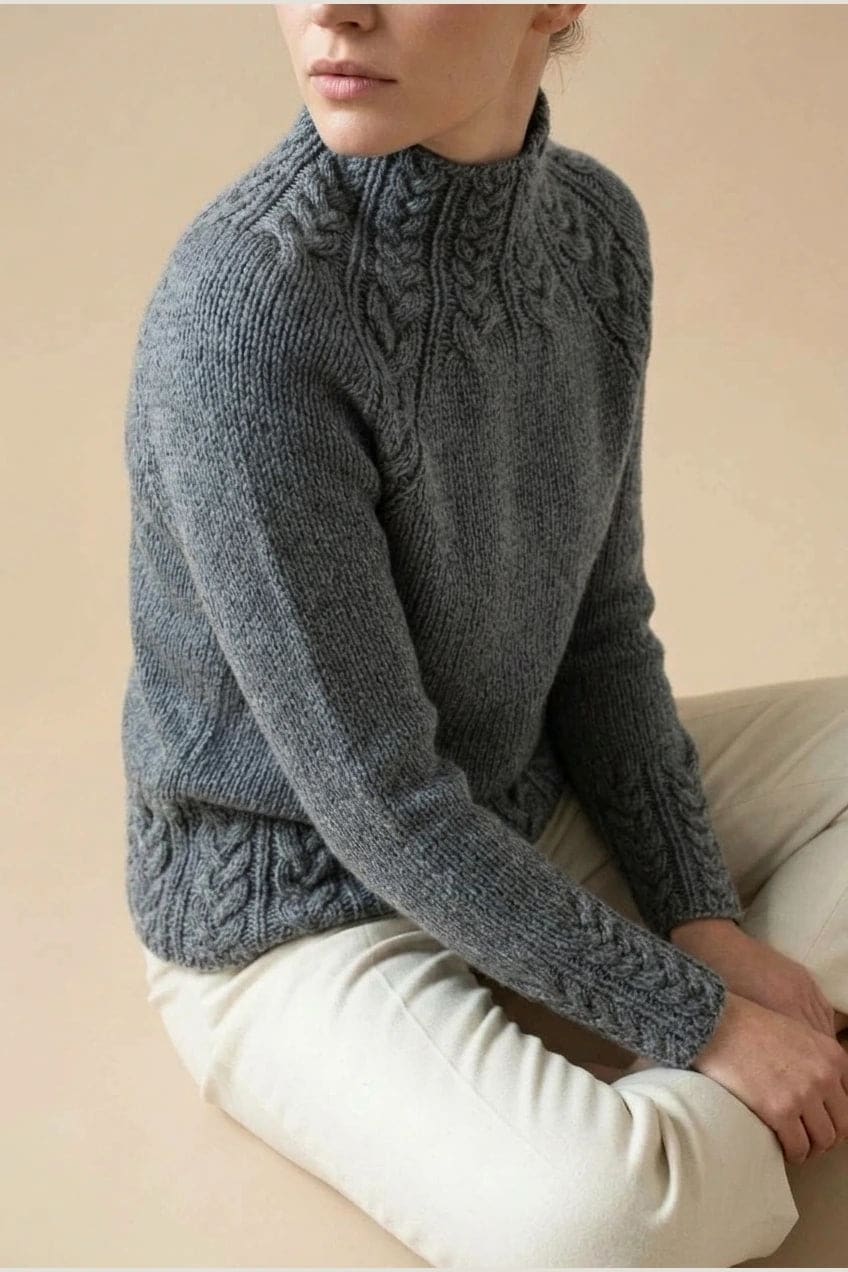 Kvinde i strikket sweater med høj hals, raglanærmer og snoningsmønster ved skuldre og nederste kant._3