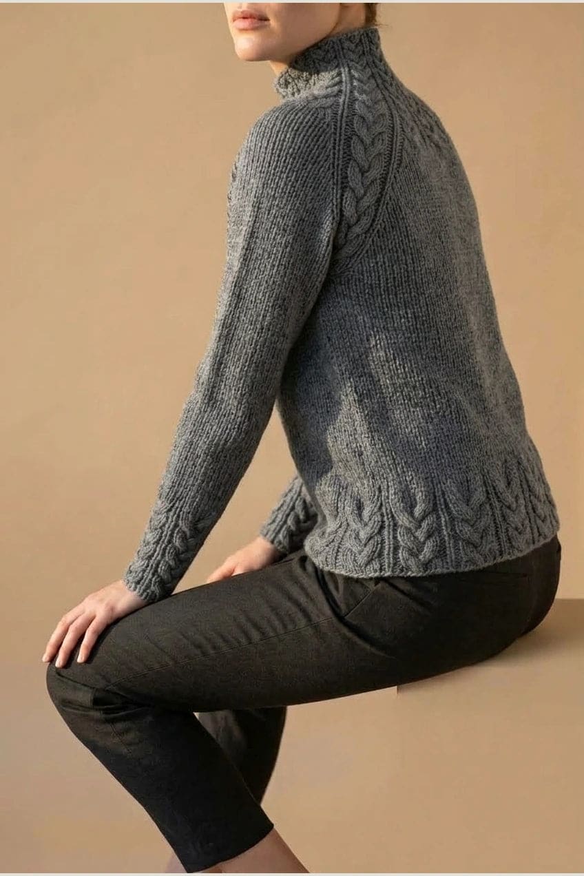 Kvinde i strikket sweater med høj hals, raglanærmer og snoningsmønster ved skuldre og nederste kant._4