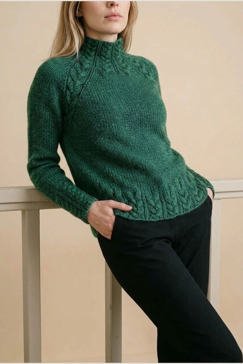 Kvinde i strikket sweater med høj hals, raglanærmer og snoningsmønster ved skuldre og nederste kant._9