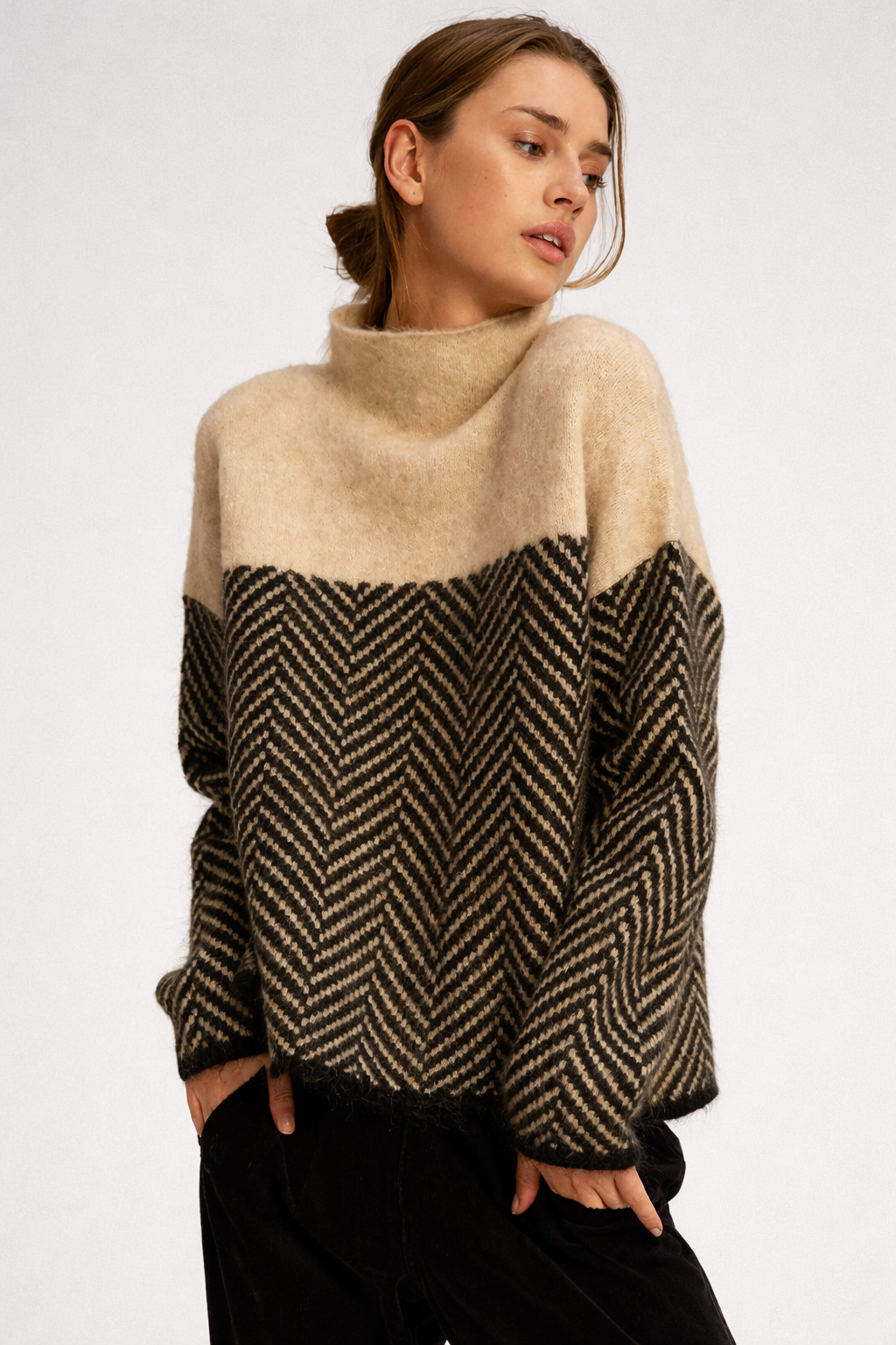 Kvinde iført en beige og sort sweater med rullekrave og chevron-mønster, stylet med lyse jeans._1
