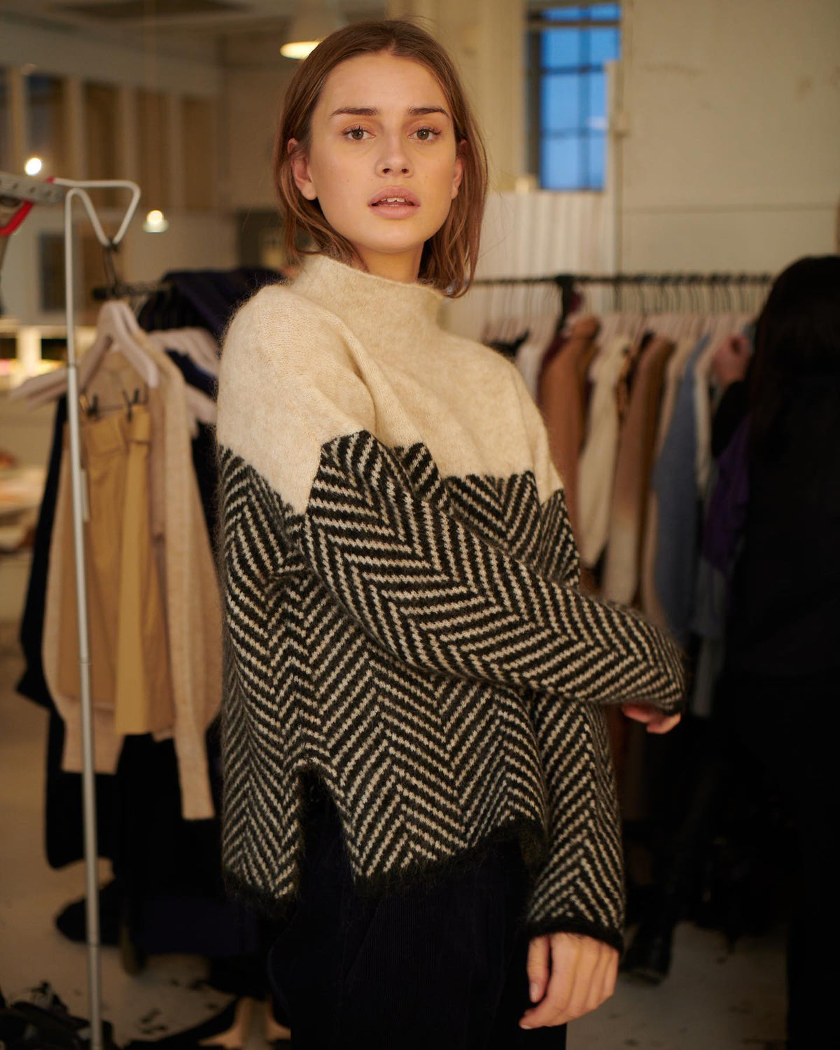 Kvinde iført en beige og sort sweater med rullekrave og chevron-mønster, stylet med lyse jeans._2