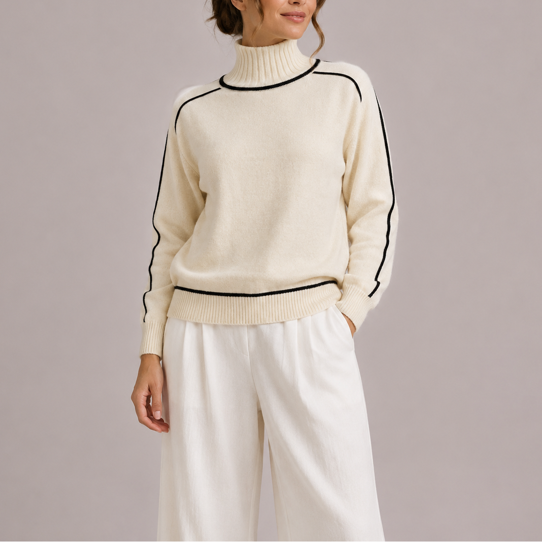 Kvinde iført en cremefarvet sweater med rullekrave og sorte kontrastdetaljer, stylet med hvide bukser._0