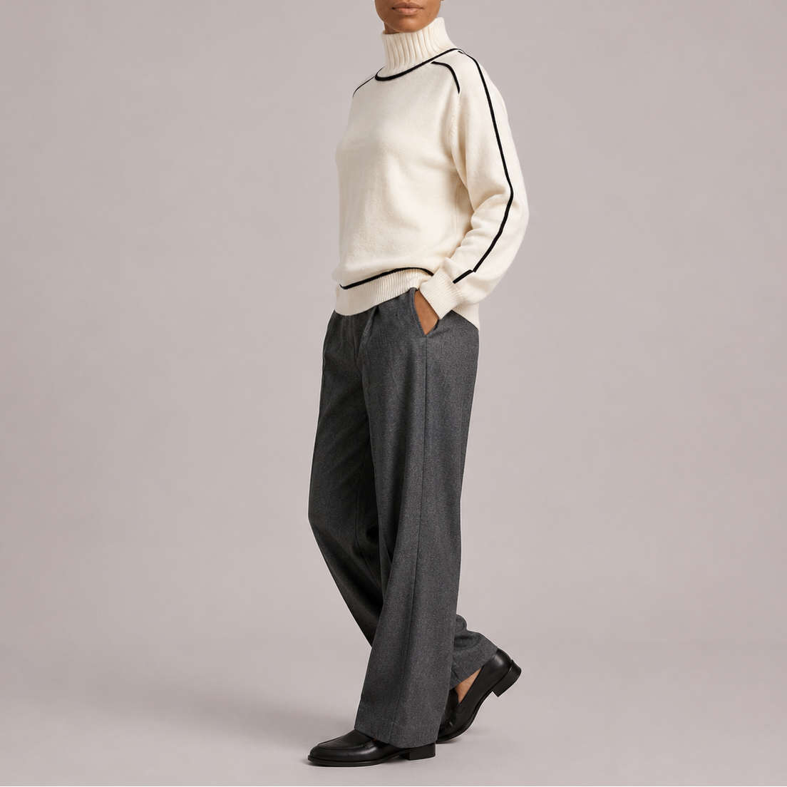 Kvinde iført en cremefarvet sweater med rullekrave og sorte kontrastdetaljer, stylet med hvide bukser._3