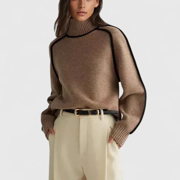 Kvinde iført en brun rullekrave sweater med kontrasterende sorte kantsømme, stylet med lyse bukser og et bælte._0