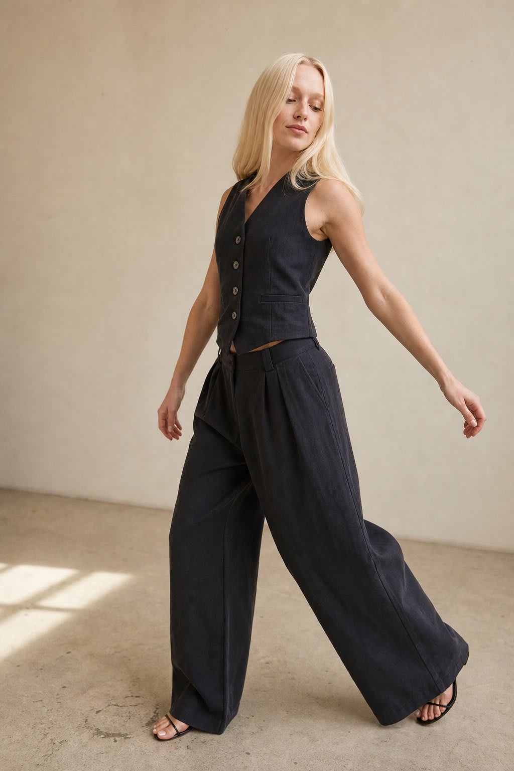 Kvinde iført todelt sæt bestående af vest med knapper og wide-leg bukser i beige nuancer, fotograferet i minimalistisk interiør_3