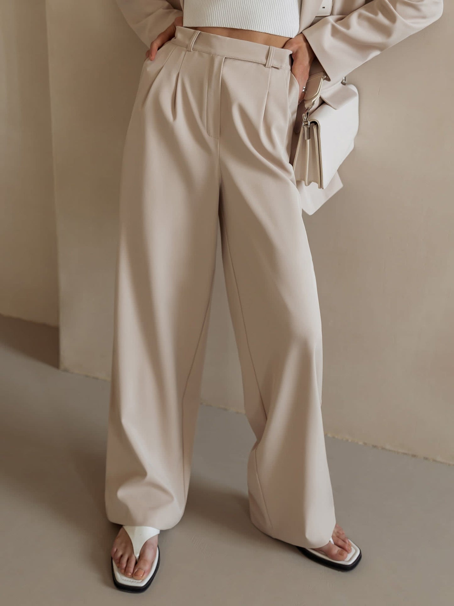 Kvinde iført lyse wide-leg bukser i høj talje, skræddersyet pasform, med cropped top og blazer._12