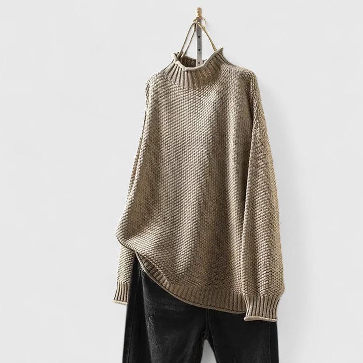 Grå strikket sweater med højhals og struktureret overflade vist på knage mod hvid baggrund_5